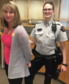 a woman standing next to a police officer in an office cubicle with a camera on her shoulder