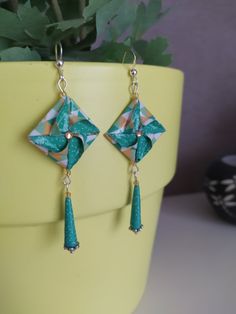 a pair of green and gold earrings sitting on top of a yellow potted plant