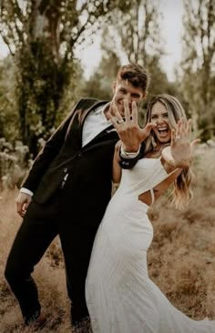 a man and woman posing for a photo in the grass with their hands up to them