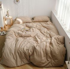 an unmade bed sitting next to a window in a room with white walls and wooden floors