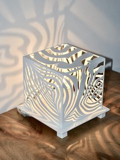 a white lamp sitting on top of a wooden table next to a shadow cast wall