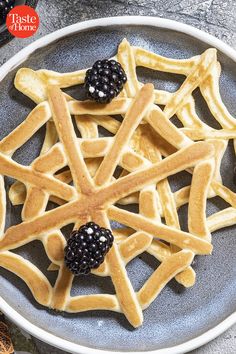 a plate with waffles and blackberries on it next to some cinnamon sticks