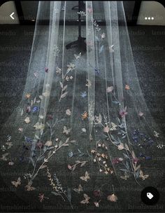 a veil with flowers and butterflies on the floor in front of a window at night