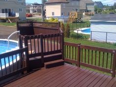 a wooden deck next to an above ground swimming pool in a residential area with houses in the background