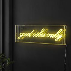 a neon sign that says good vibes only on the wall next to a potted plant