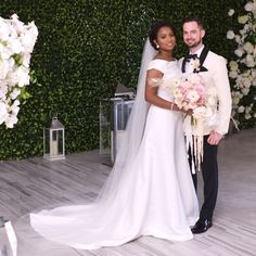 a bride and groom pose for a photo in front of a floral wall at their wedding