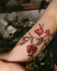 a woman's arm with pomegranates and leaves on it