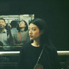 a woman standing in front of a mirror next to other people on a subway train