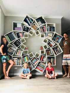 three children are sitting in front of a book shelf with books on it and two adults standing next to them