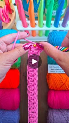 two hands are holding yarn in front of colorful crochet hooks and skeins