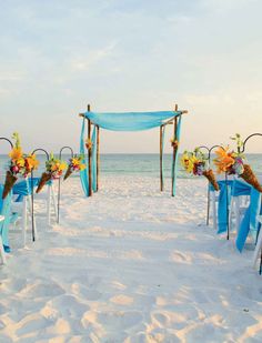 an outdoor ceremony setup on the beach with blue and yellow flowers in vases next to chairs