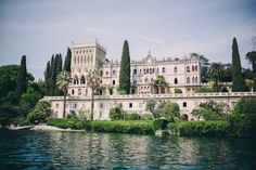 a large building sitting on top of a lush green hillside next to a lake with lots of trees