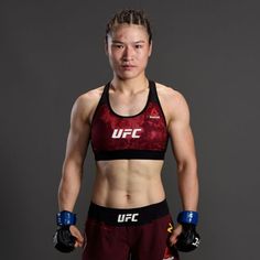 a female fighter posing for the camera with her hands on her hips and wearing boxing gloves