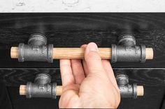 a hand holding a piece of wood in front of a black cabinet with knobs