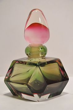 a glass bottle that is sitting on a white table top with a pink flower in it