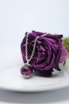 a purple rose sitting on top of a white plate next to a silver chain necklace