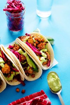 there are three tacos on the table with some guacamole and red cabbage