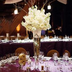 a tall vase filled with white flowers sitting on top of a table covered in wine glasses