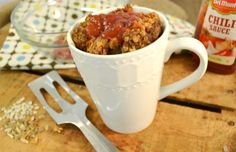 a white cup filled with food next to a fork and spoon on top of a wooden table