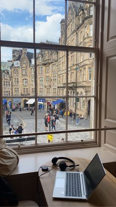 an open laptop computer sitting on top of a wooden desk next to a large window