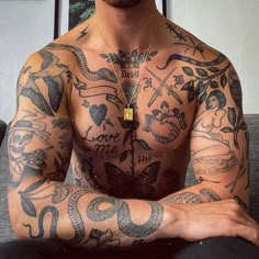 a man with lots of tattoos on his chest and arms, sitting in front of a gray couch