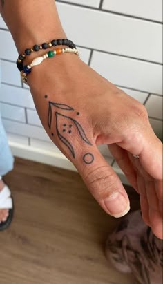 a woman's hand with a small tattoo on it and a beaded bracelet around her wrist