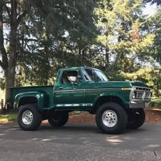 a green pick up truck parked in front of some trees