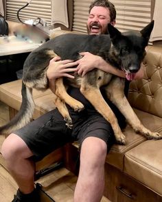 a man sitting on top of a couch holding a german shepard dog in his arms