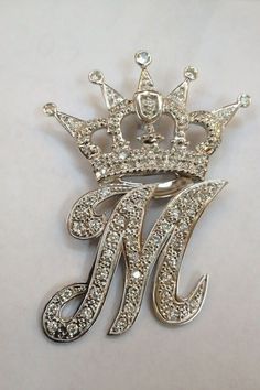 a silver brooch with a crown on it's head and the letter m