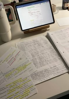 an open laptop computer sitting on top of a desk next to some papers and cups