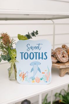 there is a sign that says sweet toothies next to some doughnuts and plants