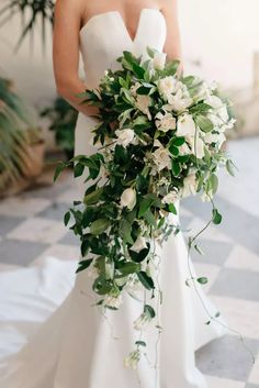 a bride holding a bouquet of white flowers and greenery