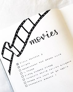 an open notebook with the words movies written on it and a film strip drawn in black ink