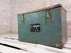 an old green trunk sitting on top of wooden pallets in front of a brick wall