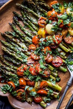 asparagus, tomatoes and other vegetables on a wooden platter with a fork