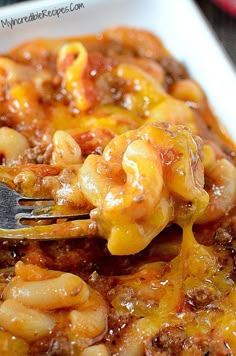 a close up of a fork in a casserole dish with meat and cheese