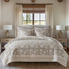 a bed in a bedroom next to two lamps and a window with beige drapes