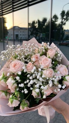 a bouquet of pink roses and white baby's breath in front of a building