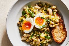 an egg sits on top of some beans in a bowl with toasted bread and green onions