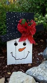 a wooden snowman with a red bow on it's head sitting next to some rocks