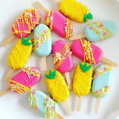 a white plate topped with colorfully decorated cookies and ice cream pops on top of wooden skewers