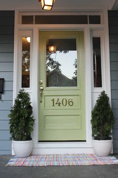 a green front door with two potted plants on the side and a light fixture above it