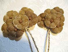 two hair pins with flowers on them sitting on a white tableclothed surface, one is brown and the other is beige