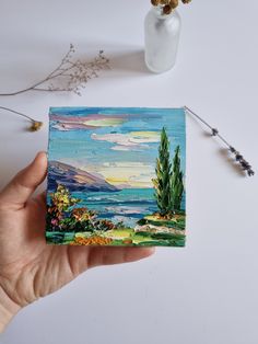 a person holding up a small painting in their hand