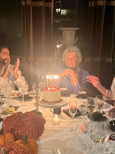 three people sitting at a table with a birthday cake