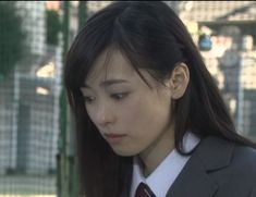 a woman in a suit and tie looking down at her cell phone while standing outside