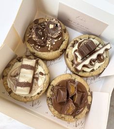 four cookies with chocolate and marshmallow toppings in a box on a table