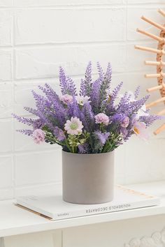 purple flowers are in a gray vase on a white table