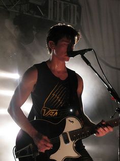 a young man playing an electric guitar in front of a microphone and spotlights on the stage