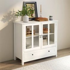 a white cabinet with glass doors and plants on top, in a living room setting